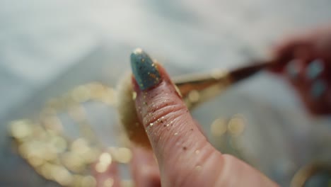 applying gold glitter to blue nails