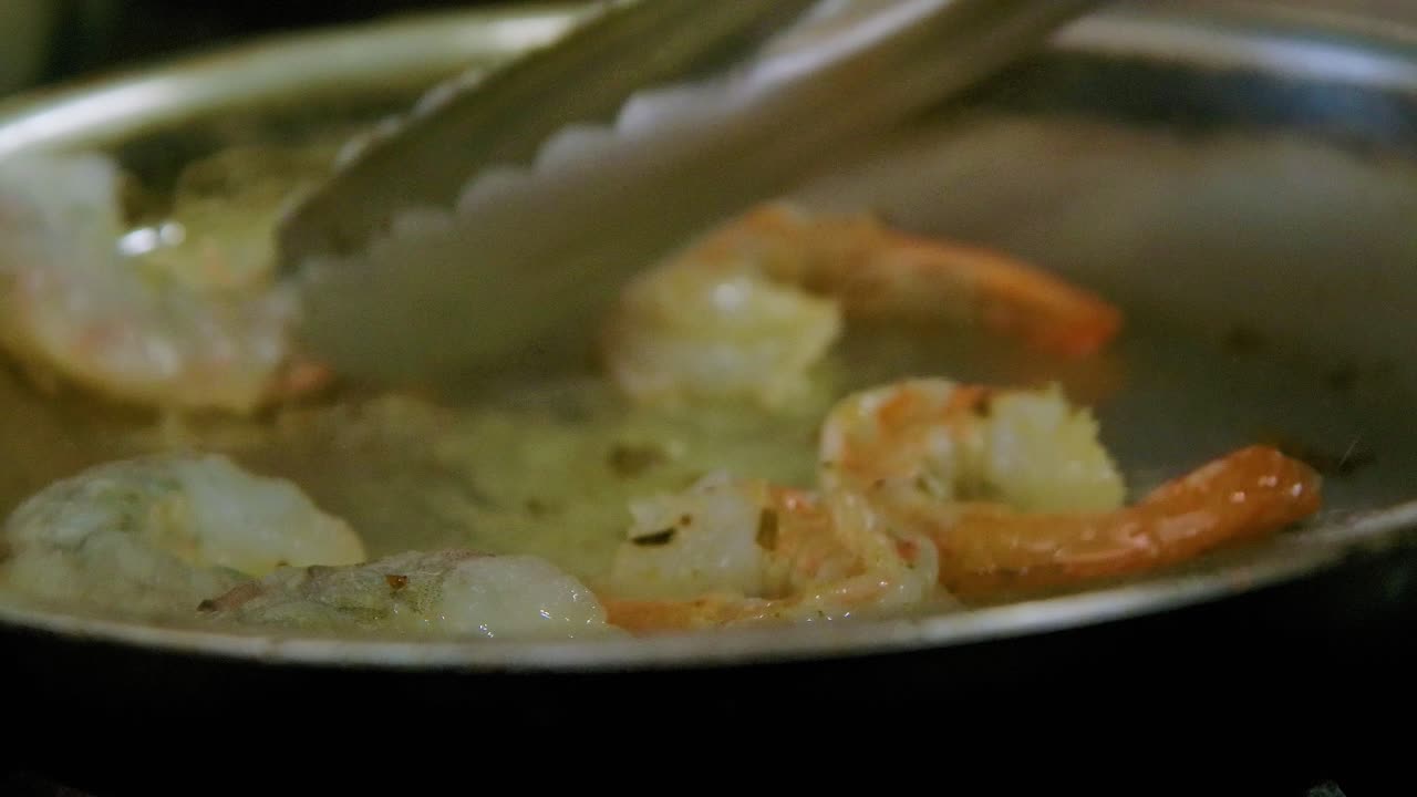 chef usando la lengua para voltear camarones en la sartén caliente