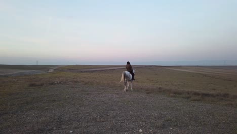 Un-Hombre-Encapuchado-Montando-Un-Caballo-Blanco-Por-La-Tarde