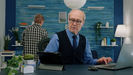 Elderly-man-using-tablet-and-laptop-in-same-time-compering-financial-graphs