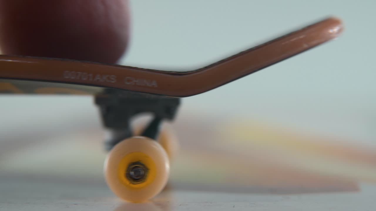 una toma macro detallada de un mini patineta, pequeñas ruedas blancas, montando fingerboard de derecha a izquierda, deslizamiento de dedos, iluminación profesional, vídeo estático cinematográfico 4k