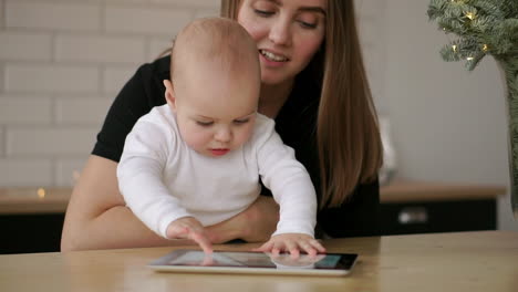 la madre y el bebé están buscando jugar y leer el ordenador de la tableta en el sofá en casa