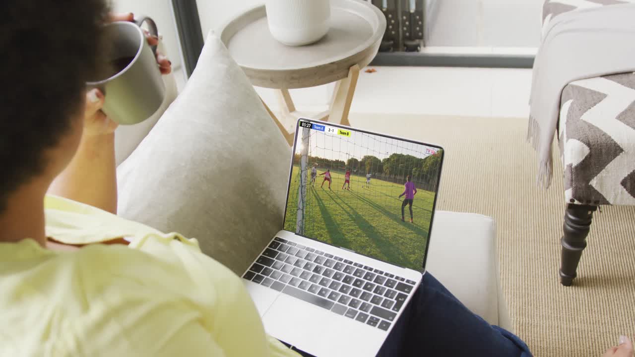 African american woman using laptop with diverse male soccer players playing match on screen