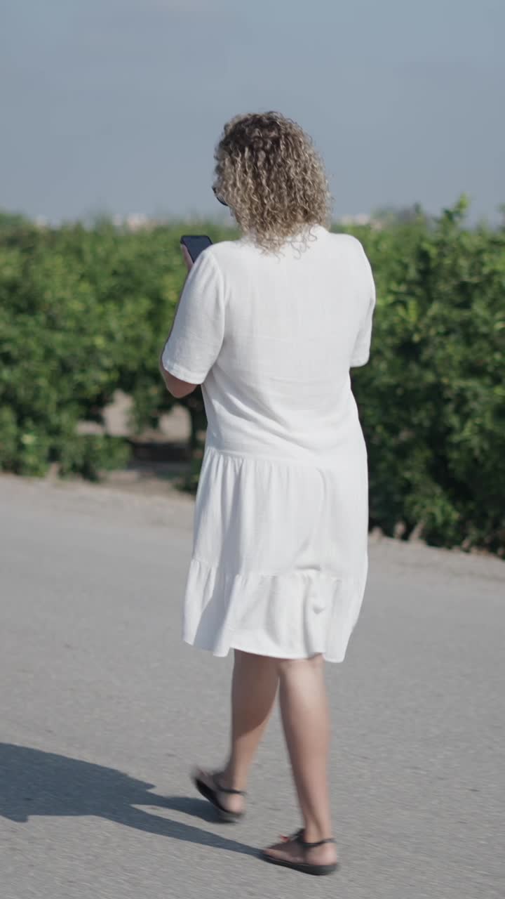 Woman in white dress walking on a road using her phone