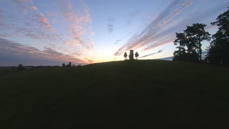 A-slow-aerial-shot-flying-over-a-hill-and-a-shrine-revealing-the-horizon-during-sunrise