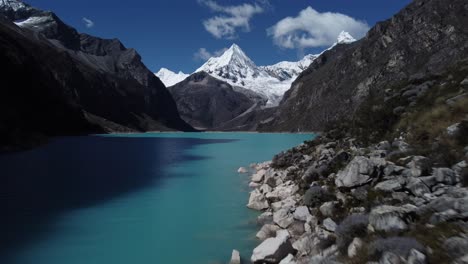 cinematic aerial shot entering a valley over a blue lagoon and a snow-capped peak at laguna parón