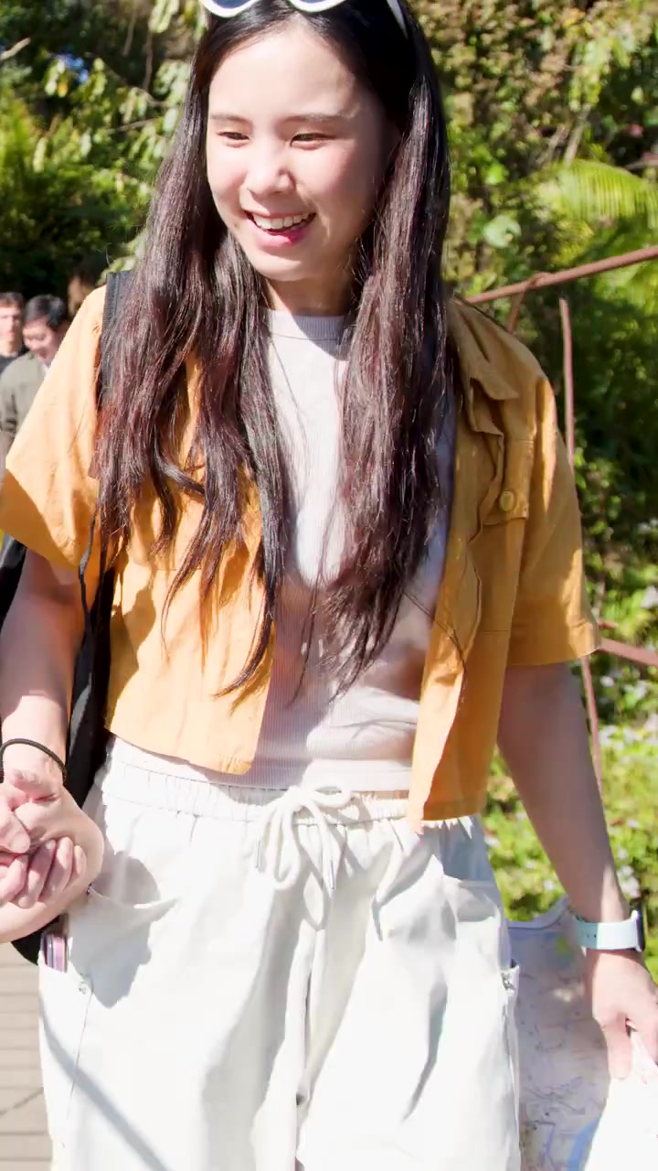 Giovane donna sorridente attraversa un ponte sospeso in una foresta soleggiata, tenendo una mappa, avventura di viaggio casual.