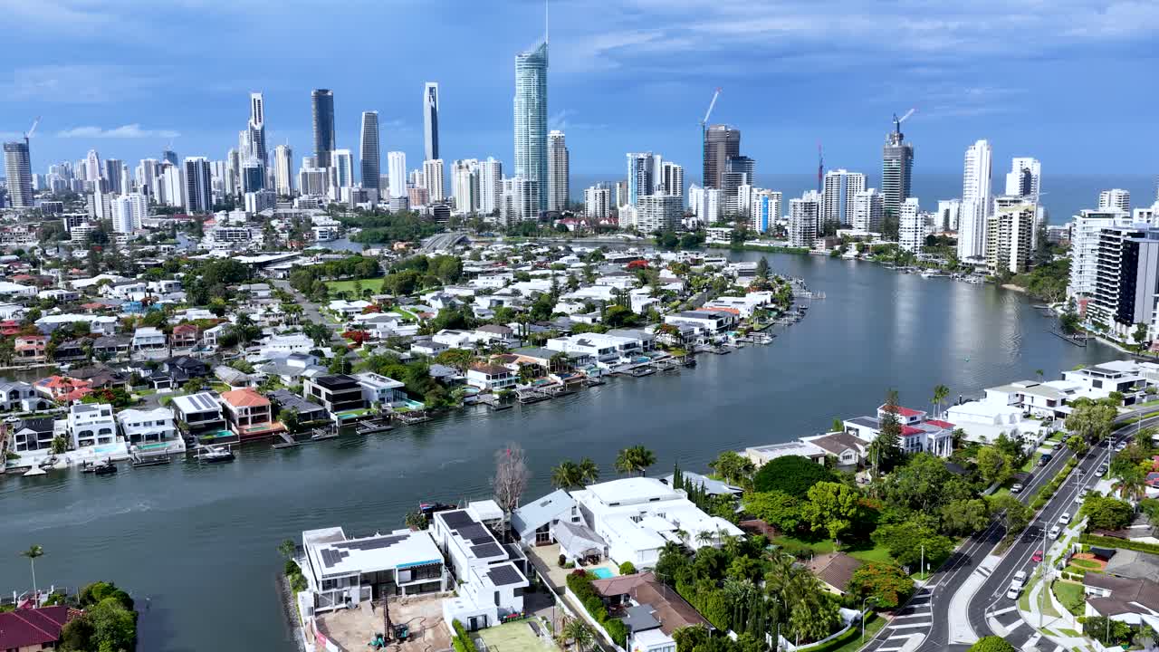 Drone glides over canal, luxury homes, marina, and city skyline in bright daylight