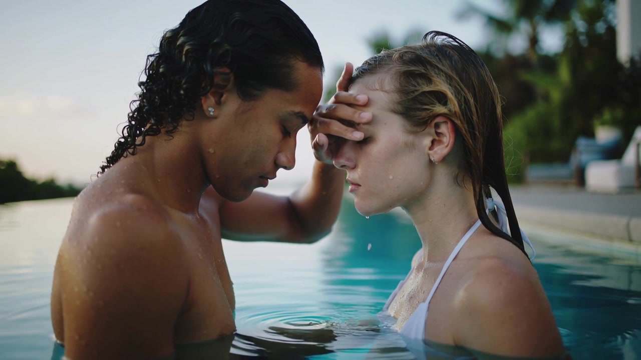 Raising hand man placing palm on woman's brow, calming her in pool, white-bikini-top, drops falling