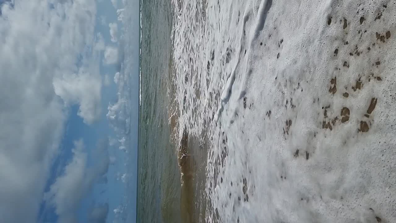 ondas del océano tropical en movimiento lento vertical que fluyen sobre una playa de arena dorada bajo un cielo nublado azul
