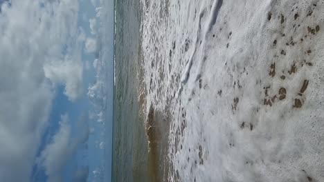 Olas-Oceánicas-Tropicales-En-Cámara-Lenta-Vertical-Que-Fluyen-Sobre-Una-Playa-De-Arena-Dorada-Bajo-Un-Cielo-Azul-Nublado