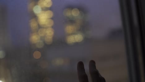 mano tocando una ventana con vistas a la ciudad por la noche