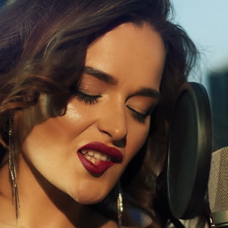 passionate model is singing next to the microphone iin the sound studio. close-up face of beautiful singer woman with perfect makeup at mic looking at camera.