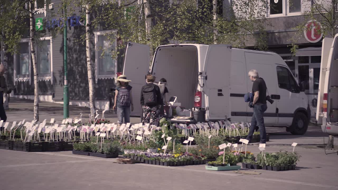 Wide shot of people buying fresh flowers from street market in Tromso during sunny day.