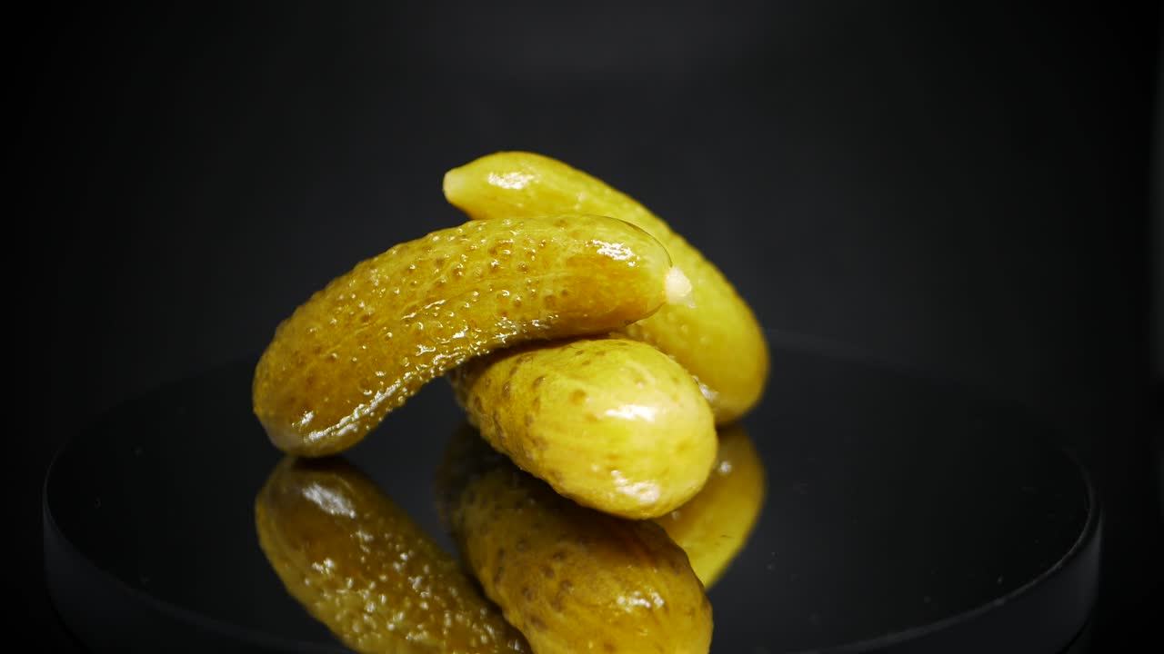 Tre syltede agurker spinner over svart bakgrunn – fermenterte agurker