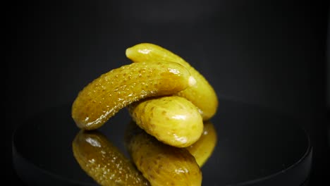 three pickled gherkins spinning over black background - fermented cucumbers