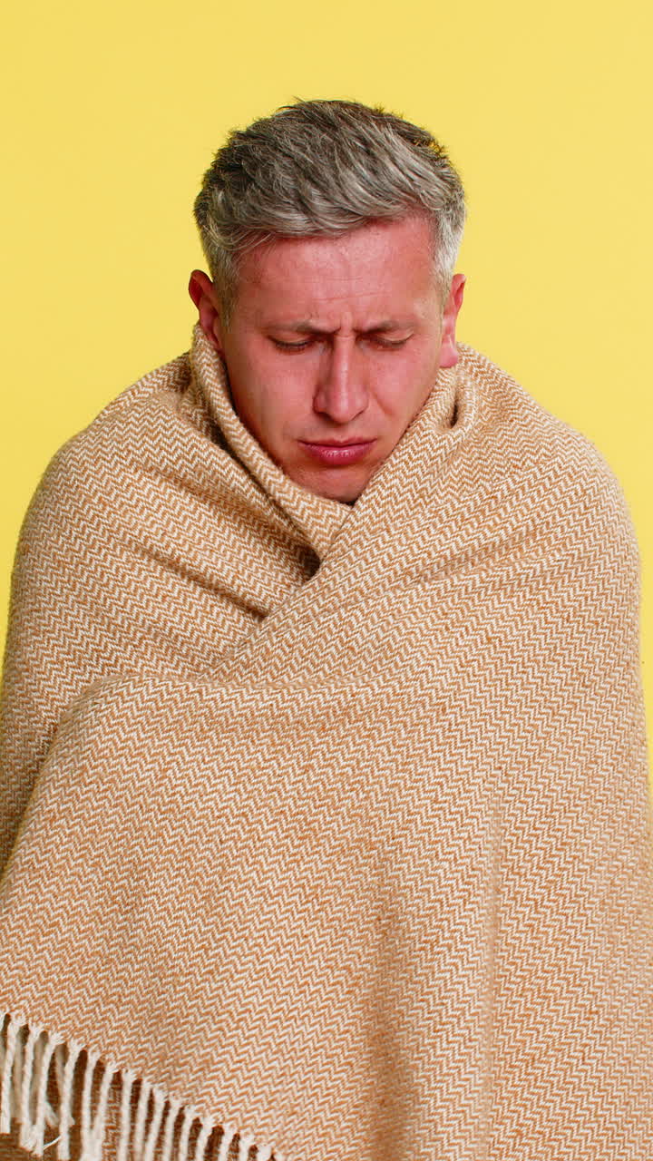 Uomo adulto avvolto in una coperta che tossisce con un'espressione stanca e sofferente, che mostra sintomi di influenza, raffreddore e virus