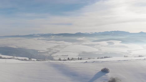 left flying aerial over snowed-in hill with mountain range in backdrop