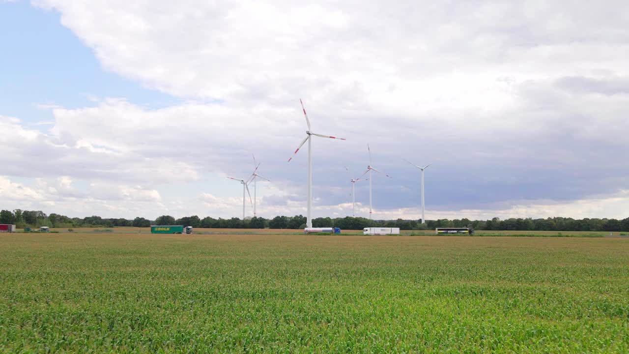 Drone footage of wind turbines beside a highway, surrounded by farmland and cornfields