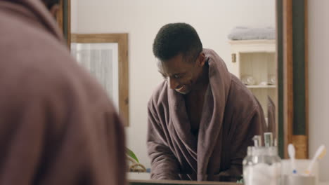 happy african american man dancing in bathroom looking in mirror having fun morning routine getting ready enjoying positive self image wearing bathrobe