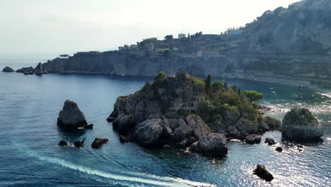 A-boat-near-a-rocky-island-with-coastal-cliffs-in-italy,-aerial-view