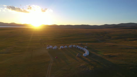 Vista-Aérea-De-Yurtas-A-Lo-Largo-De-La-Orilla-Del-Lago-Song-kul-Mientras-El-Sol-Se-Pone-En-El-Vasto-Desierto-De-Kirguistán