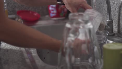 persona enjuagando vasos, cucharas y un trapo en el fregadero de la cocina - estático, tiro medio