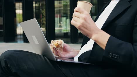a businessman eating a sandwich while working on his laptop