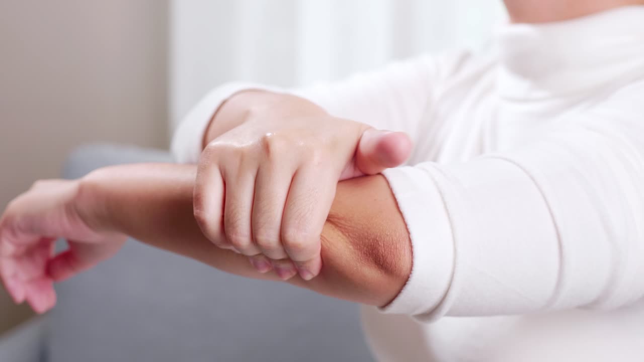 mujer joven que tiene dolor en el codo y usa la mano para automasaje para aliviar dolores y molestias