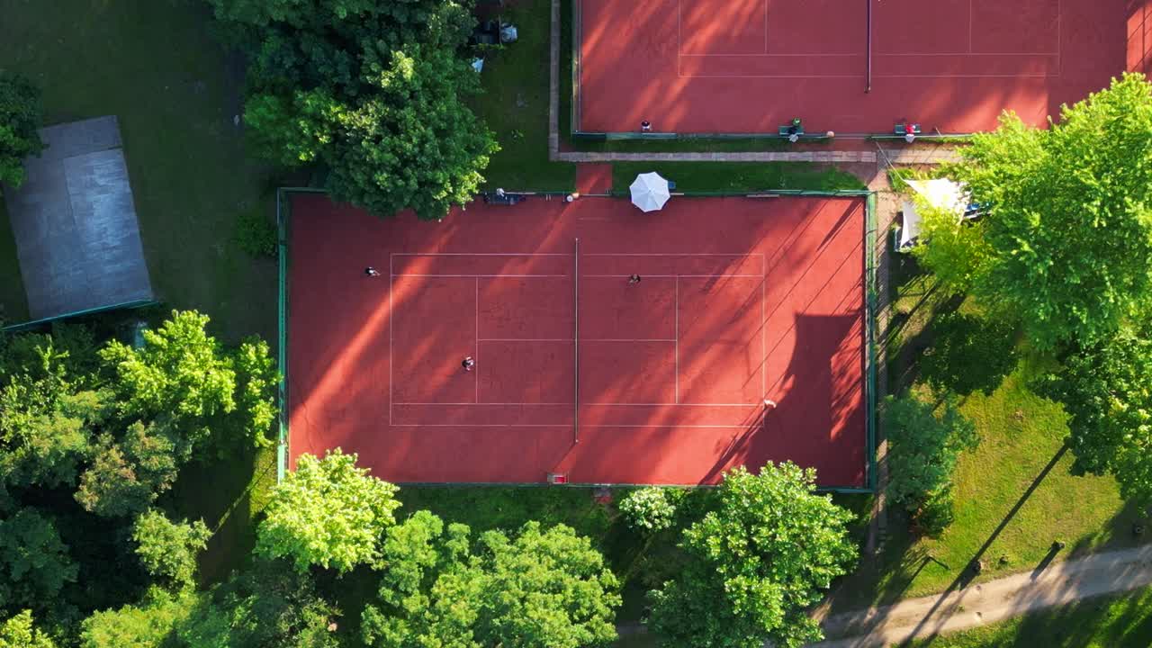 Persone che giocano una partita a tennis su campi in terra battuta durante una giornata di sole a Berlino, Germania. Drammatica vista aerea, volo verticale a volo d'uccello con drone.