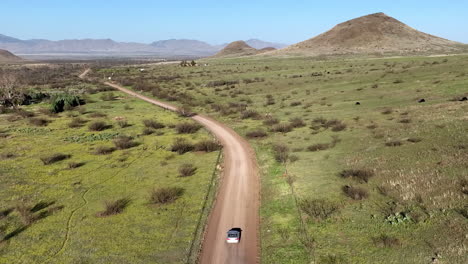 Aerial-shot-of-car-on-dirt-road-in-Willcox,-Arizona,-wide-tracking-drone-shot-with-mountains-in-the-background