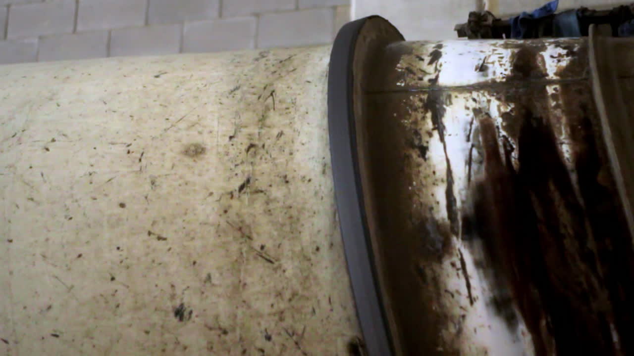 Close-up of a dirty industrial metal drum or cement mixer showing grease, rust, and wear marks in a construction environment. Emphasis on texture and machinery detail