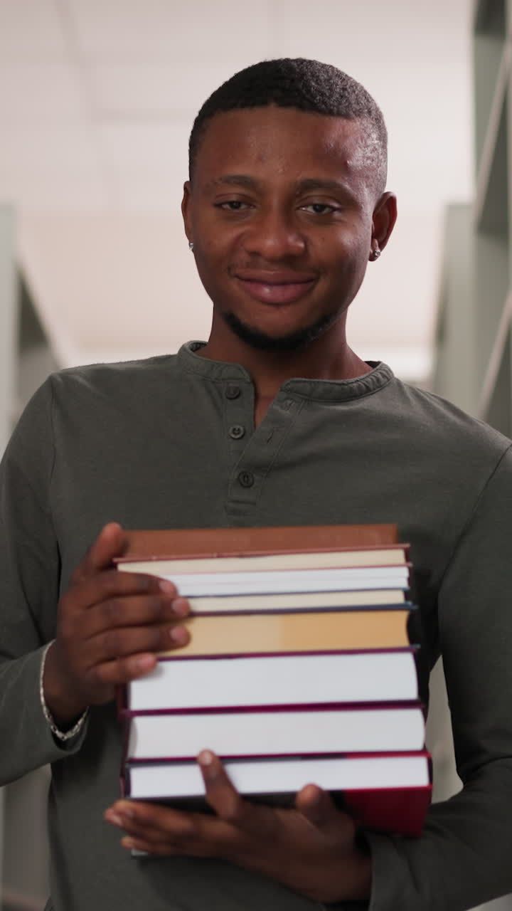 Positive teacher holds books in school library. African American student prepares literature stack to do homework in bookstore. Black guy with folios