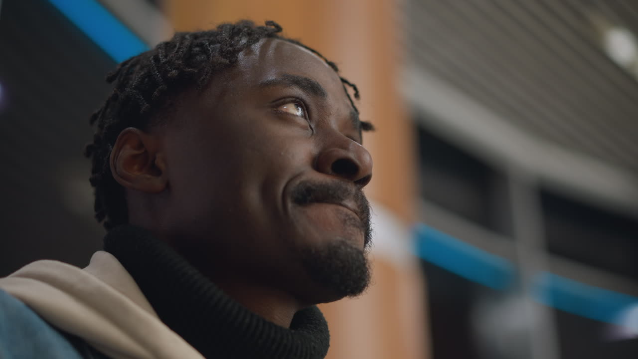 Confident young man holding paper cup, sipping beverage with calm expression, looking upward in modern indoor space, enjoying peaceful moment and reflecting on his thoughts