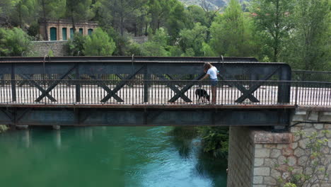 一位年轻的女人和她的狗走过一座古老的铁桥,lago de bolarque