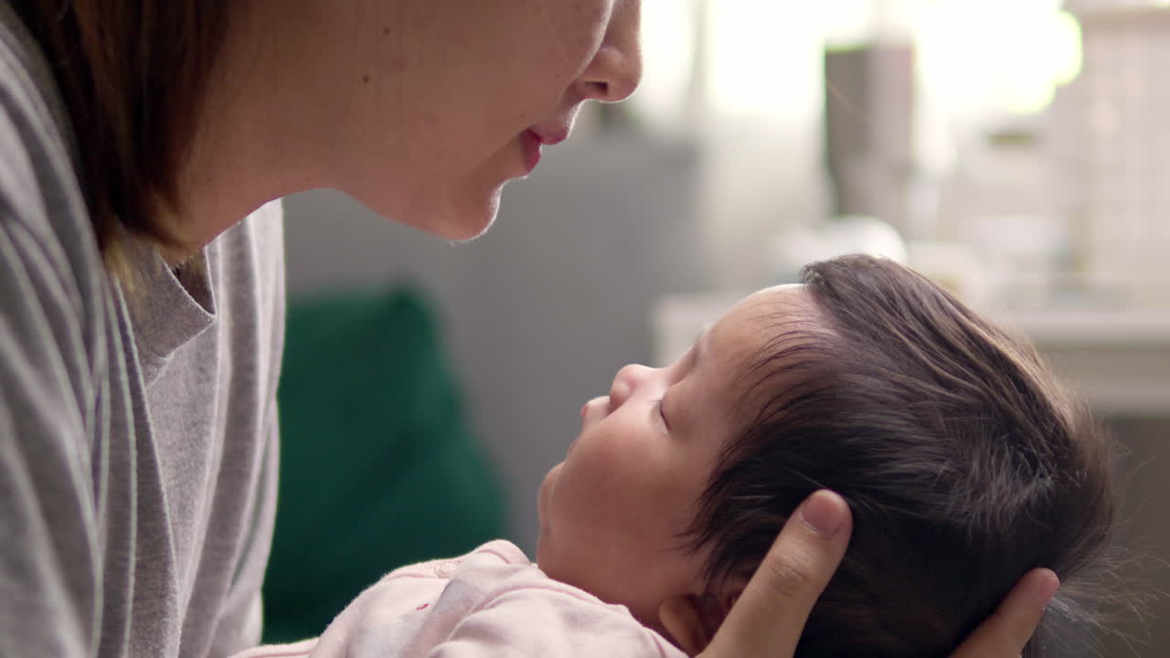 Mother approaching face to face of sleeping newborn baby.