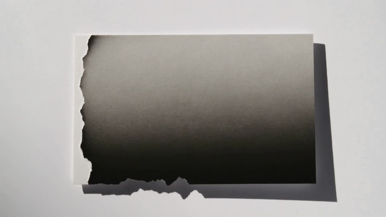 Showing rectangular card filling dark gradient from torn lower edge on white table, casting shadow