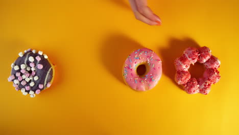 multiple child hands quickly grab all four colorful donuts—chocolate marshmallow, blue frosted with gummy shark, pink sprinkle, and strawberry mochi—from a vibrant yellow background playful.