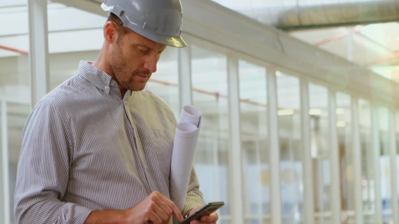 Caucasian male engineer with blueprint plan using smartphone at construction site