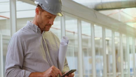 Ingeniero-Masculino-Caucásico-Con-Plan-De-Proyecto-Usando-Un-Teléfono-Inteligente-En-El-Sitio-De-Construcción