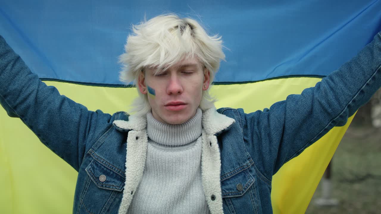 кавказский мужчина держит украинский флаг и смотрит в камеру.