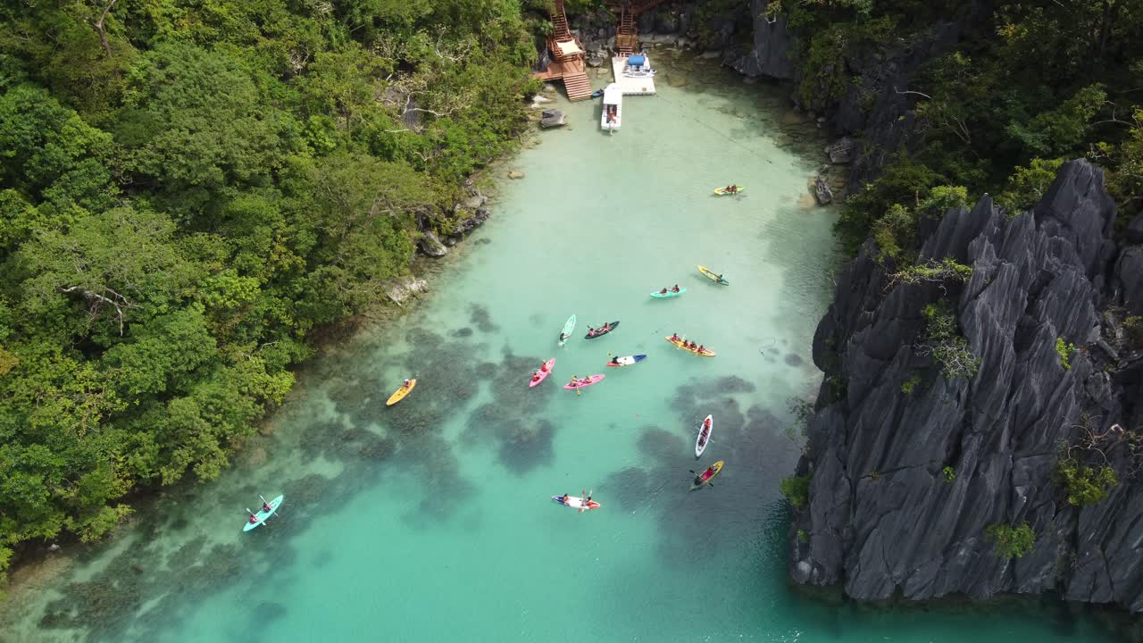 People sea kayaking on turquoise blue water of tropical Cadlao Lagoon in El Nido