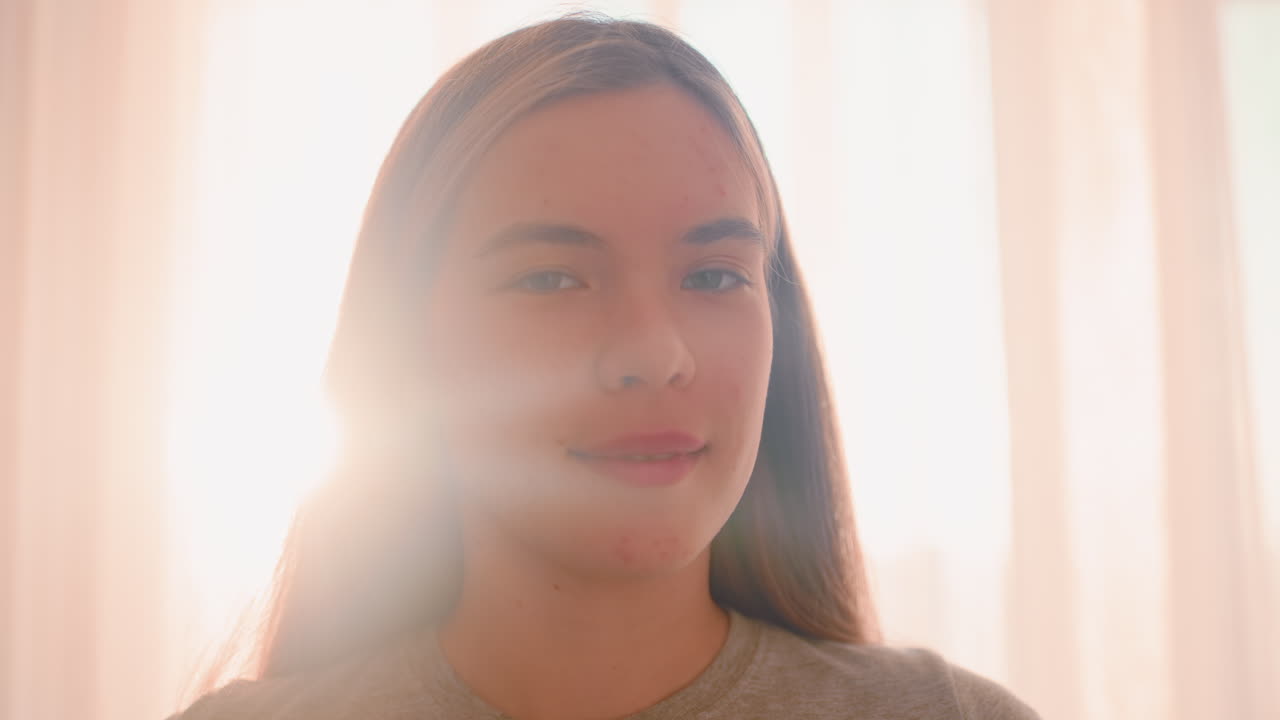 Close up of lady with warm smile standing in front of curtain as sunlight streams through fabric, highlighting natural face with spots and creating soft glowing atmosphere indoors