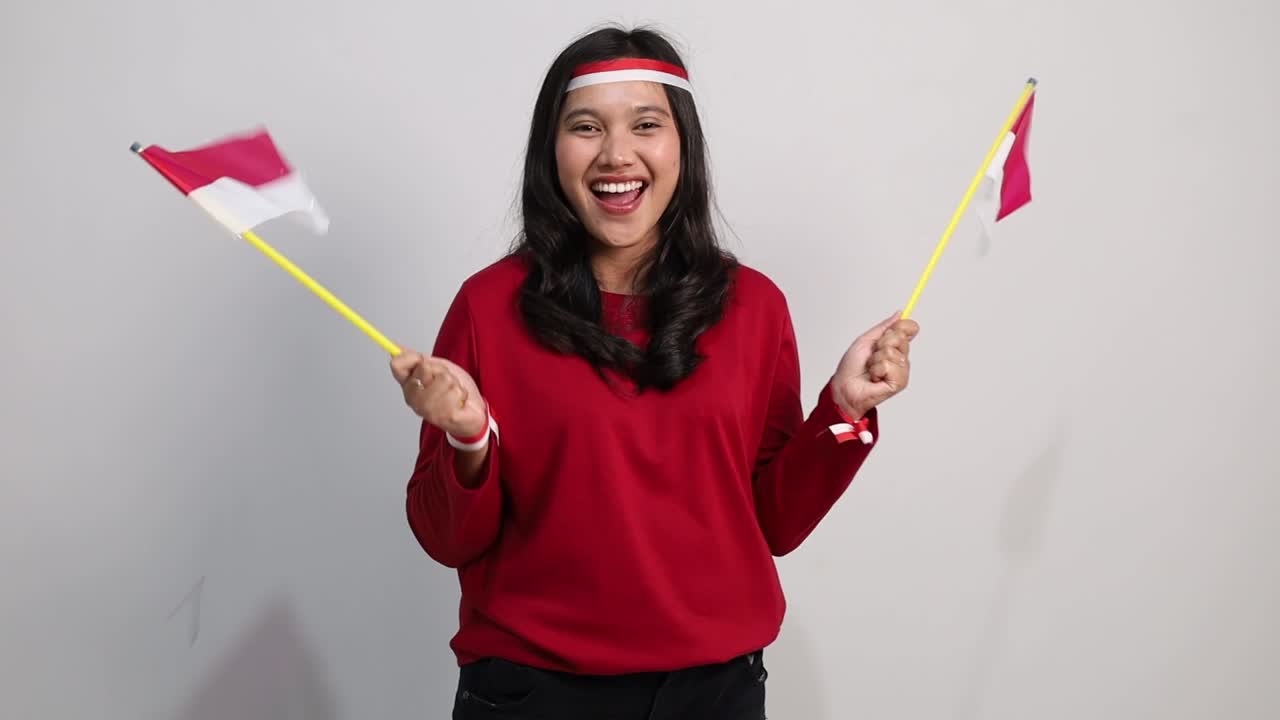 Giovane donna indonesiana allegra in piedi che tiene la bandiera rossa e bianca per celebrare il giorno dell'indipendenza dell'Indonesia.