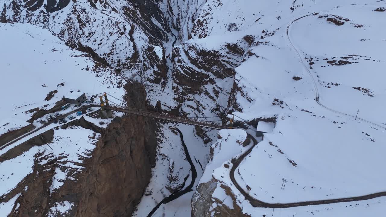 Aerial view of a suspension bridge in a snowy mountain valley