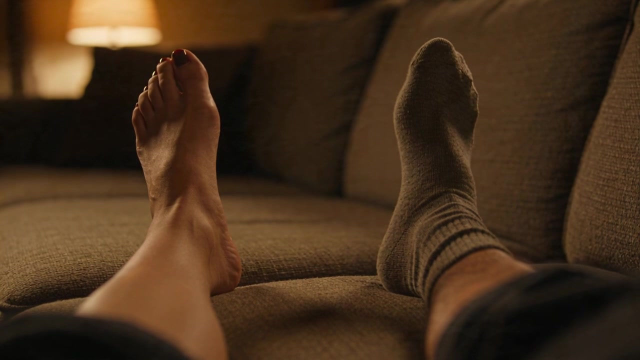 Resting, left bare foot flexing on sofa, painted toenails and right foot wearing gray crew sock