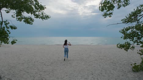 Mujer-Caminando-Lejos-De-La-Cámara-En-La-Playa-Nublada-En-El-Condado-De-Prince-Edward,-Ontario,-Canadá