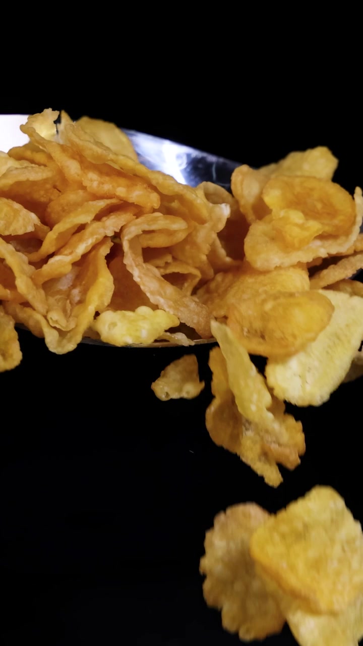 Cornflakes drop from a spoon, captured in slow motion against a dark backdrop, highlighting their texture and movement