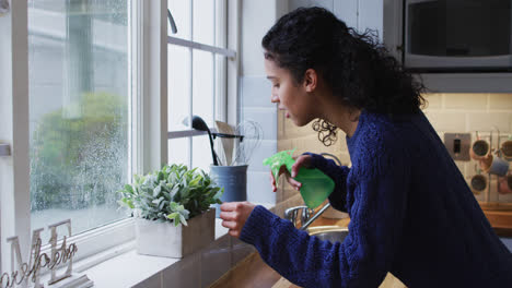 mixed race woman watering plants in kitchen