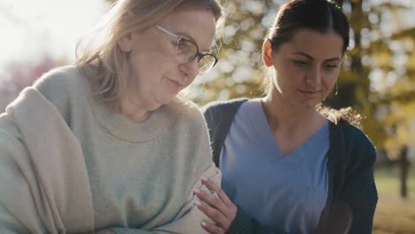 young female nurse helping senior woman walking in park